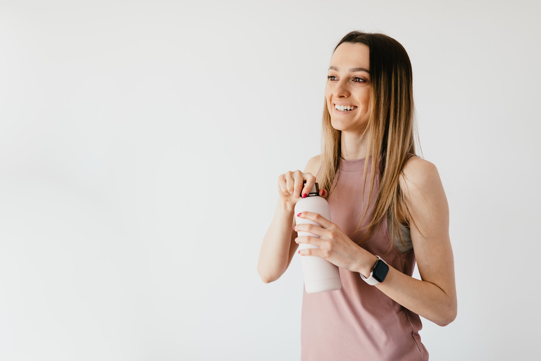 happy young woman opening cosmetic bottle while standing against white background