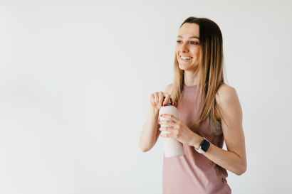 happy young woman opening cosmetic bottle while standing against white background
